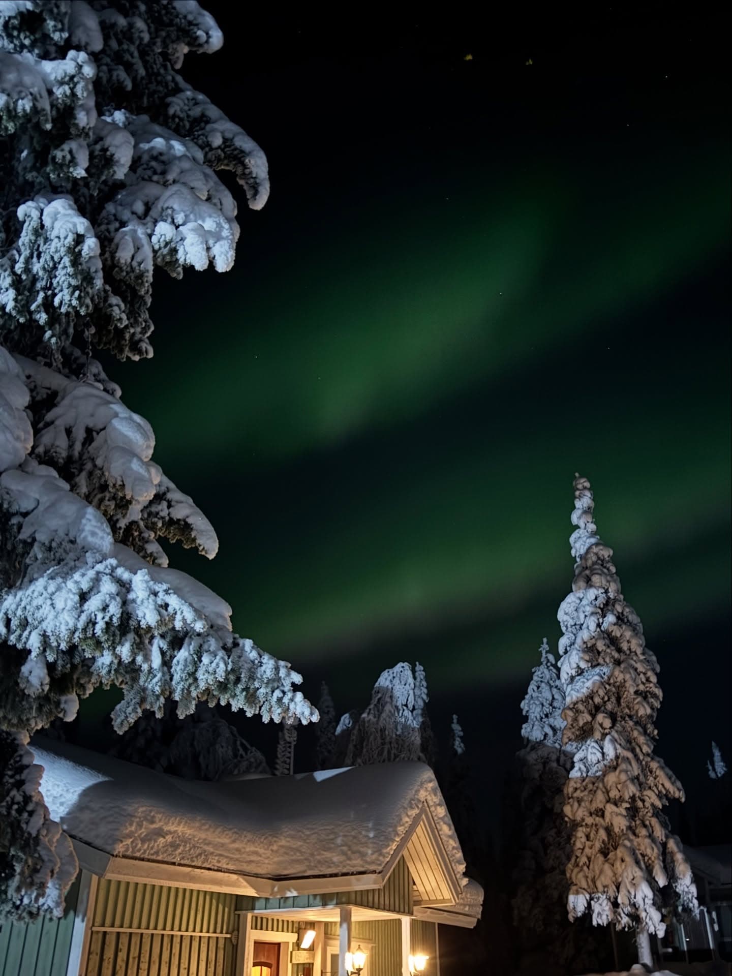 Green aurora borealis dancing above a Kettura Finland cabin in deep snow